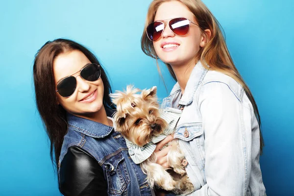 Lifestyle and people concept: Two young girl friends standing together and holding dog — Stock Photo, Image