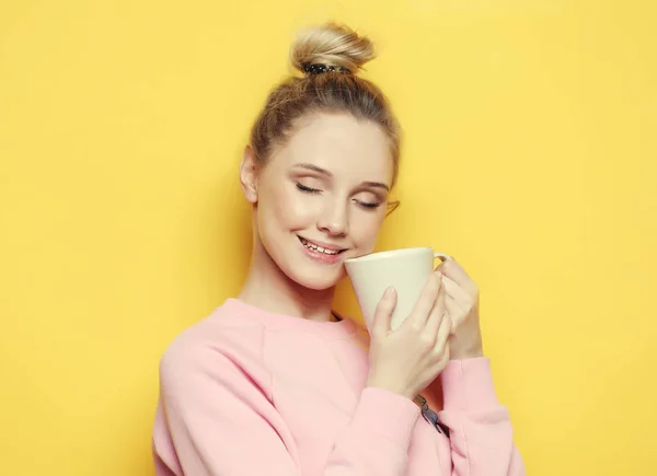Молода блондинка тримає білу чашку з чаєм або кавою, способом життя та концепцією їжі. Жовтий фон . — стокове фото