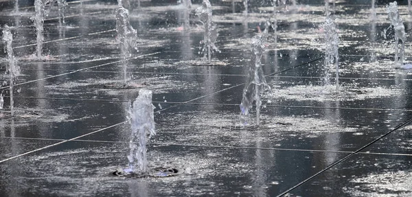 Pequeña fuente hermosa en el aire libre, en la calle. Gotas de agua, chorros de agua congelados en el aire en vuelo contra el telón de fondo. día de verano . — Foto de Stock