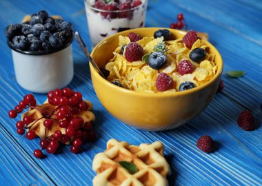 Çilek Ahududu ve mavi ahşap arka plan üzerinde yaban mersini ile Mısır gevreği.