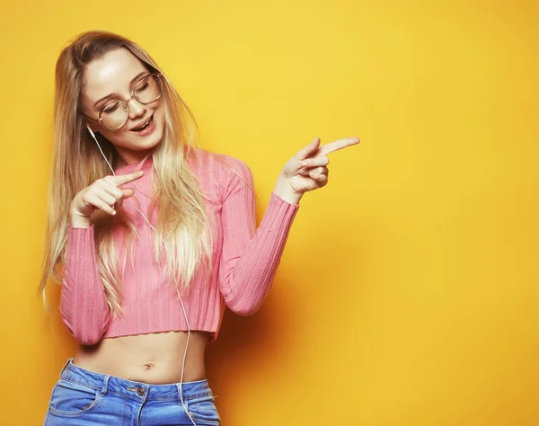 Lifestyle and people concept - Portrait of a pretty blond girl pointing finger away over yellow background — Stock Photo, Image