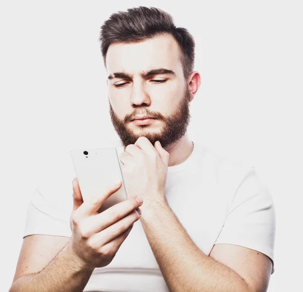 Junger Mann schaut auf sein Smartphone, während er auf weißem Hintergrund isoliert SMS schreibt — Stockfoto