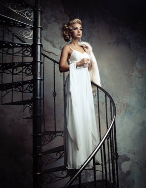 Beyaz elbiseli güzel genç gelin bir döner merdiven üzerinde duruyor. Düğün kavramı.