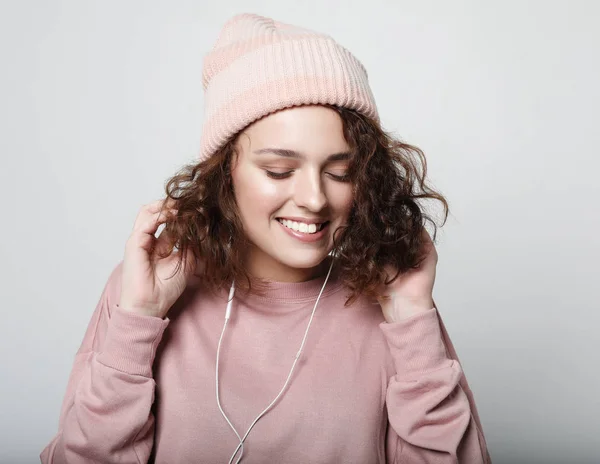 Lifestyle en mensen concept: Mooie jonge krullende vrouw in hoofdtelefoon luisteren naar muziek glimlachen met gesloten ogen staan op witte achtergrond in een roze sweatshirt. — Stockfoto