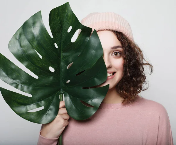 Mladá krásná žena v růžové ležérní oblečení, drží list monstera, pózovat na bílém pozadí — Stock fotografie