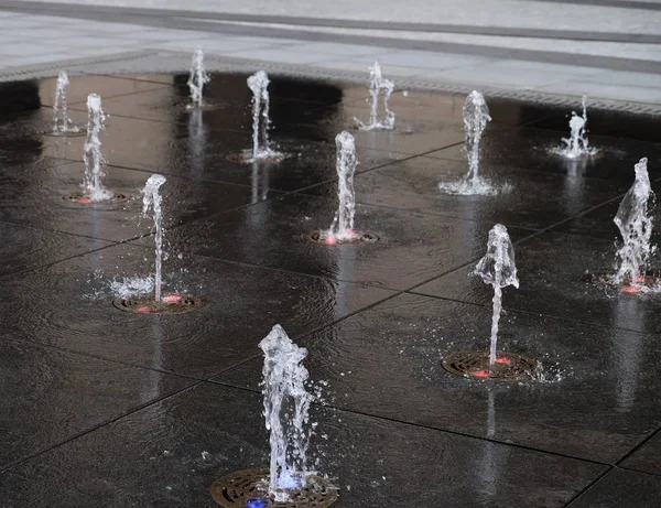 Pequeña fuente hermosa en el aire libre, en la calle. Gotas de agua, chorros de agua congelados en el aire en vuelo contra el telón de fondo . — Foto de Stock