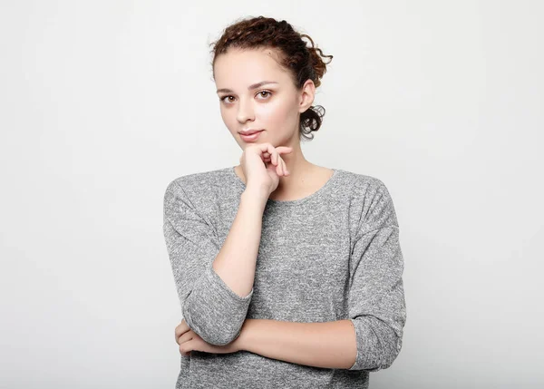 Beautiful young woman with curly hair smiling gently while listening to interesting conversation, wearing grey long-sleeved sweater, keeping arms folded. Lifestyle concept. — Stock Photo, Image