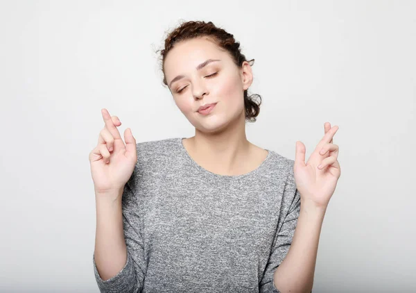 Estilo de vida y el concepto de la gente: Estudio de toma de la joven estudiante tiene una expresión esperanzadora, cruza los dedos en anticipación de anunciar resultados importantes, esperanzas de buena suerte durante la sesión . — Foto de Stock