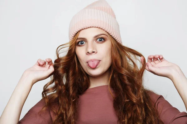 Gloomy young woman dressed casually making faces at camera, blinking, sticking out her tongue. Positive girl having fun indoors — Stock Photo, Image