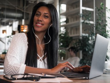 Yaşam tarzı ve insan konsepti: cep telefonu ve dizüstü bilgisayar kullanarak bir kafede mutlu bir Afrikalı kadının portresi