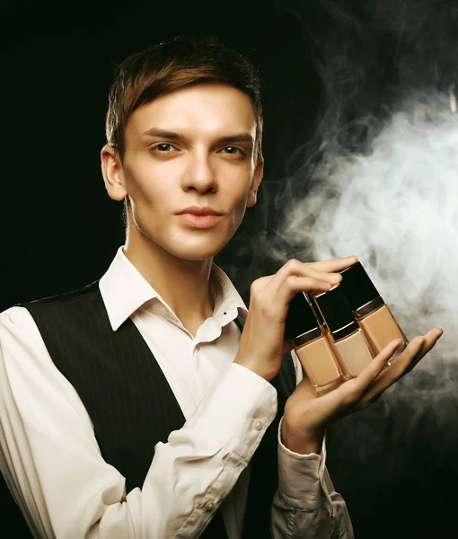 Beauty concept. Young male make up artist posing with foundation for make-up on a dark background. — Stock Photo, Image