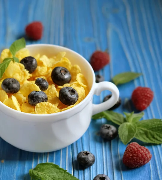 Alimentación saludable, comida y dieta - Copos de maíz con bayas frambuesas y arándanos sobre fondo de madera azul . — Foto de Stock