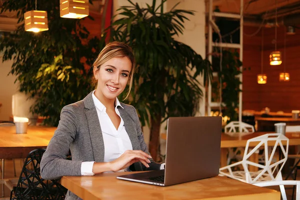 Una joven atractiva mujer de negocios sentada en un café con una computadora portátil — Foto de Stock