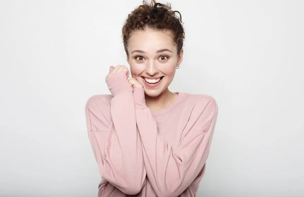 Pretty beautiful woman with curly hair looking at camera having excited and happy facial expression, against blank studio wall — Stock Photo, Image