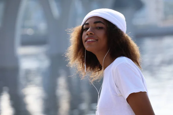 Jeune fille afro-américaine près de la mer et le pont à l'aide de téléphone mobile et écouteurs — Photo