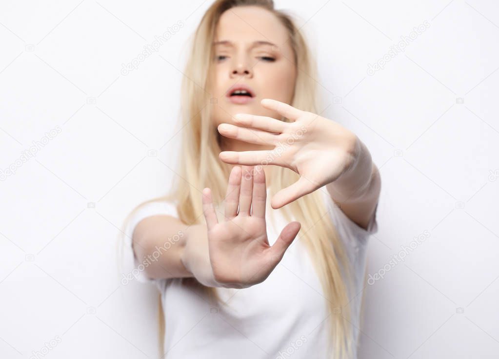 Body language. Disgusted stressed out angry young blond woman posing at studio wall, keeping hands in stop gesture, trying to defend herself as if saying: Stay away from me