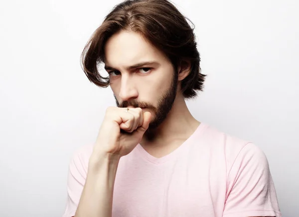 Giovane bel maschio con barba, baffi e acconciatura alla moda, indossa casual t-shirt rosa, ha una seria espressione mentre ascolta l'interlocutore — Foto Stock