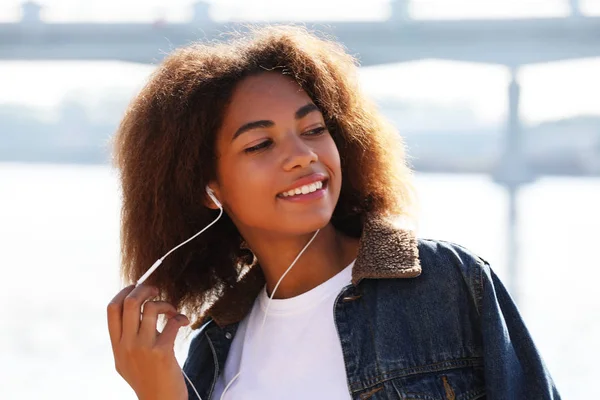 Концепция образа жизни: молодая африканская американская девушка с помощью мобильного телефона и наушников, улыбающаяся — стоковое фото