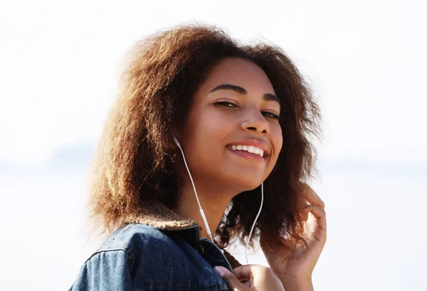 Koncepcja stylu życia: Młoda afrykańska dziewczyna używająca telefonu komórkowego i słuchawek, uśmiechnięta — Zdjęcie stockowe