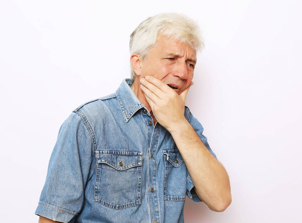 Health issues problems, people and sickness concept - studio shot of unhappy senior man pressing cheek trying to soothe toothache, having mournful painful facial expression.