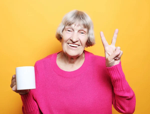 Portrét staré vzrušené dámy usmívající se, držící šálek pít kávu, čaj, nápoj na žlutém pozadí — Stock fotografie