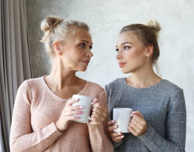 Güzel olgun anne ve yetişkin kızı kahve içiyor, konuşuyor ve gülümsüyor.