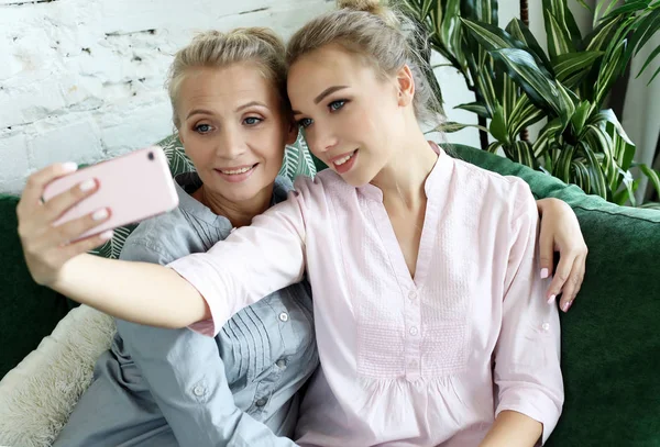 Retrato de una hermosa madre madura y su hija haciendo una selfie usando un teléfono inteligente y sonriente, hogar y feliz. —  Fotos de Stock