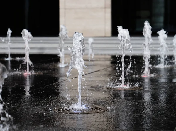 Pequeña fuente al aire libre, en la calle. Gotas de agua, chorros de agua congelados en el aire en vuelo contra el telón de fondo . — Foto de Stock