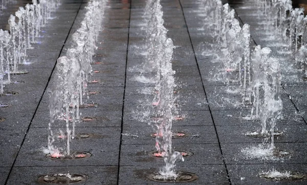 Pequeña fuente hermosa en el aire libre, en la calle. Gotas de agua, chorros de agua congelados en el aire en vuelo contra el telón de fondo. de cerca — Foto de Stock