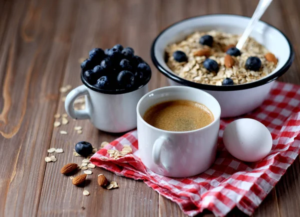 Um café da manhã saudável é um ótimo começo para um novo dia. Mingau de aveia, café, bagas e nozes em uma mesa de madeira . — Fotografia de Stock