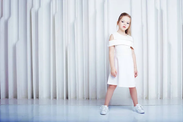 かわいい小さなのブロンドの女の子は白の背景に白のカジュアルな服を着てします。ファッションのスタイル. — ストック写真