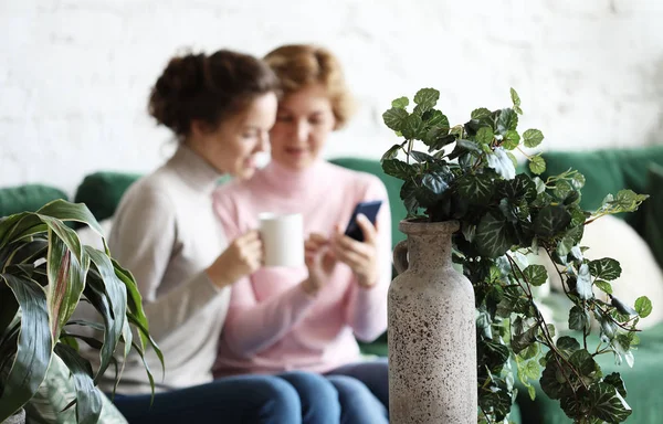Estilo de vida e conceito de pessoas: Duas mulheres bonitas- mãe e filha sentados no sofá em casa. Eles bebem café, chá. Relacionamentos e tempo compartilhado . — Fotografia de Stock