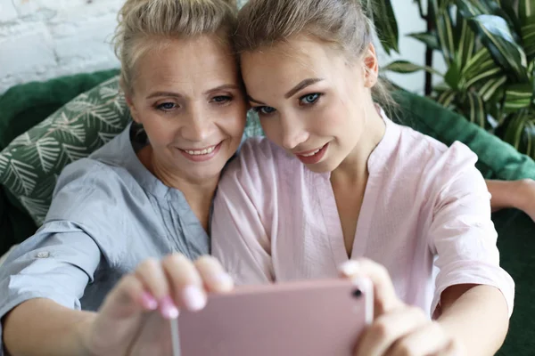 Πορτρέτο της όμορφης ώριμης μητέρας και της κόρης της κάνοντας μια selfie χρησιμοποιώντας έξυπνο τηλέφωνο και χαμογελώντας, σπίτι και ευτυχισμένη. — Φωτογραφία Αρχείου