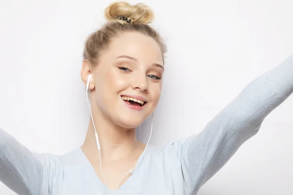 Chica rubia en auriculares escuchando música tomando fotos hace autorretrato en el teléfono inteligente con una ropa casual — Foto de Stock