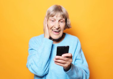 Yaşam tarzı, teknoloji ve insanlar konsepti: Yaşlı nine akıllı telefonuna bakıyor ve şaşırıyor