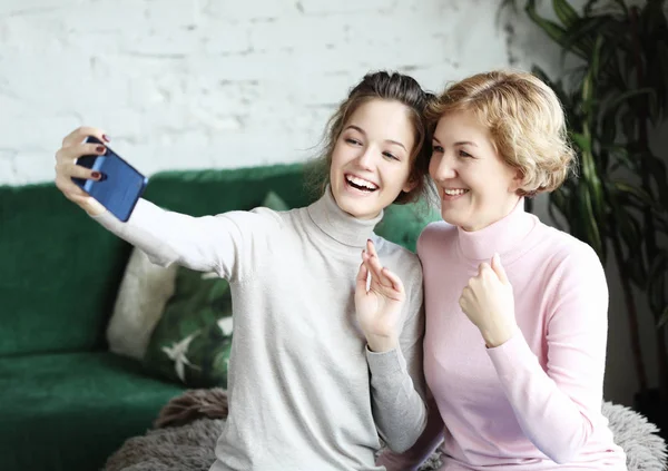 Portrett av en vakker, moden mor og datteren som lager en selfie ved hjelp av smarttelefon og smiler, hjem og er lykkelig. – stockfoto