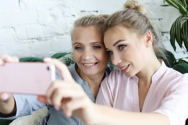 Ritratto di bella madre matura e sua figlia fare un selfie utilizzando smartphone e sorridente, a casa e felice. — Foto Stock