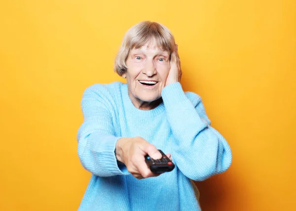 Lifestyle en mensen concept: grappige oma houdt een tv-afstandsbediening over gele achtergrond — Stockfoto