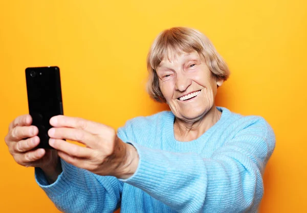 Livsstil, människor och tehnology koncept: mormor i blå tröja ler och tar en selfie — Stockfoto