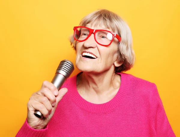 Estilo de vida y el concepto de la gente: Retrato de la abuela divertida con suéter rosa sostiene el micrófono — Foto de Stock