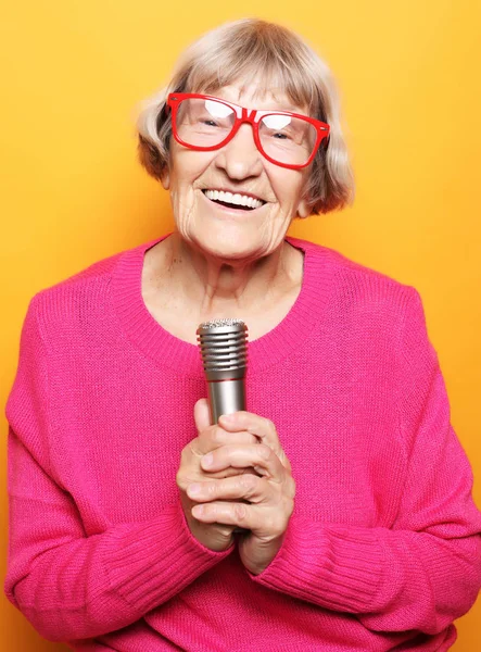 Koncepcja życia i ludzi: portret śmieszne babci różowym swetrze trzyma mikrofon — Zdjęcie stockowe