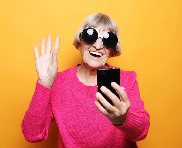 Stara babcia rozmawia przez telefon ze swoimi wnukami, uśmiecha się i wita je. — Zdjęcie stockowe