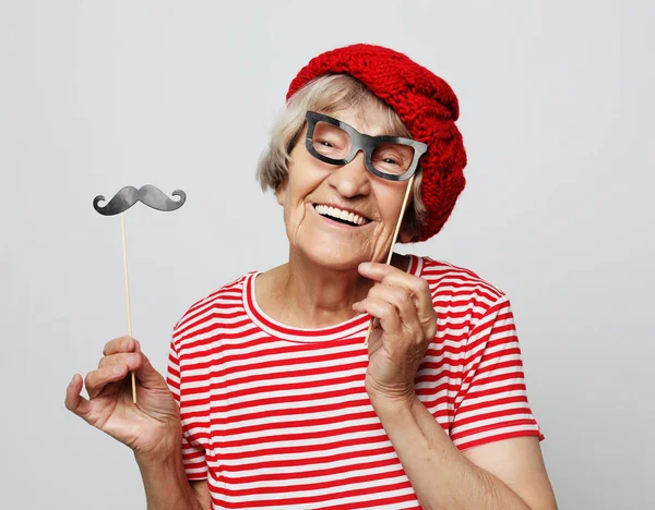 ライフスタイルと人々のコンセプト:偽物の口ひげと眼鏡を持つ面白い祖母、笑いとパーティーの準備 — ストック写真