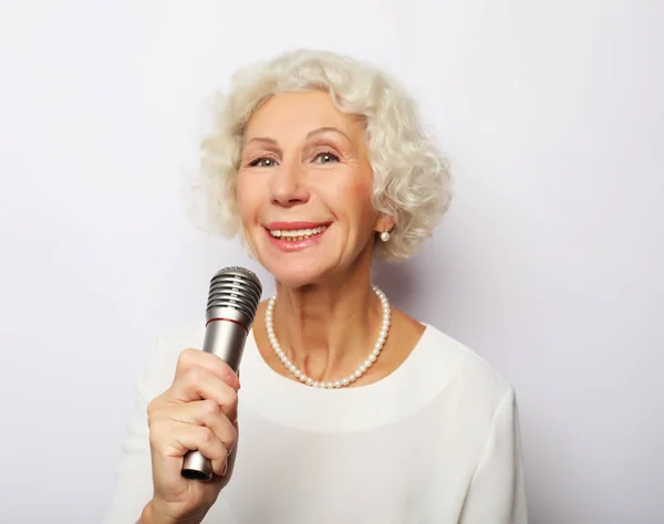 Estilo de vida y el concepto de la gente: Retrato de la encantadora abuela moderna sostiene el micrófono — Foto de Stock