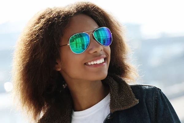 Mulher bonita usando óculos de sol com dentes perfeitos e pele limpa escura tendo descanso ao ar livre, sorrindo depois recebeu boas notícias positivas . — Fotografia de Stock