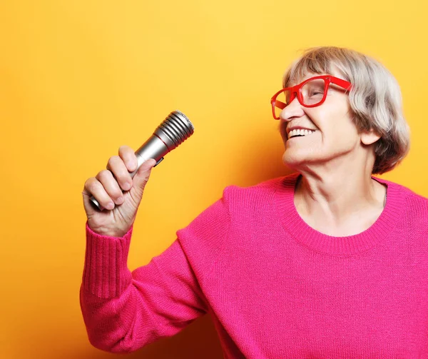 Retrato de la abuela divertida con suéter rosa sostiene el soporte del micrófono y canta —  Fotos de Stock