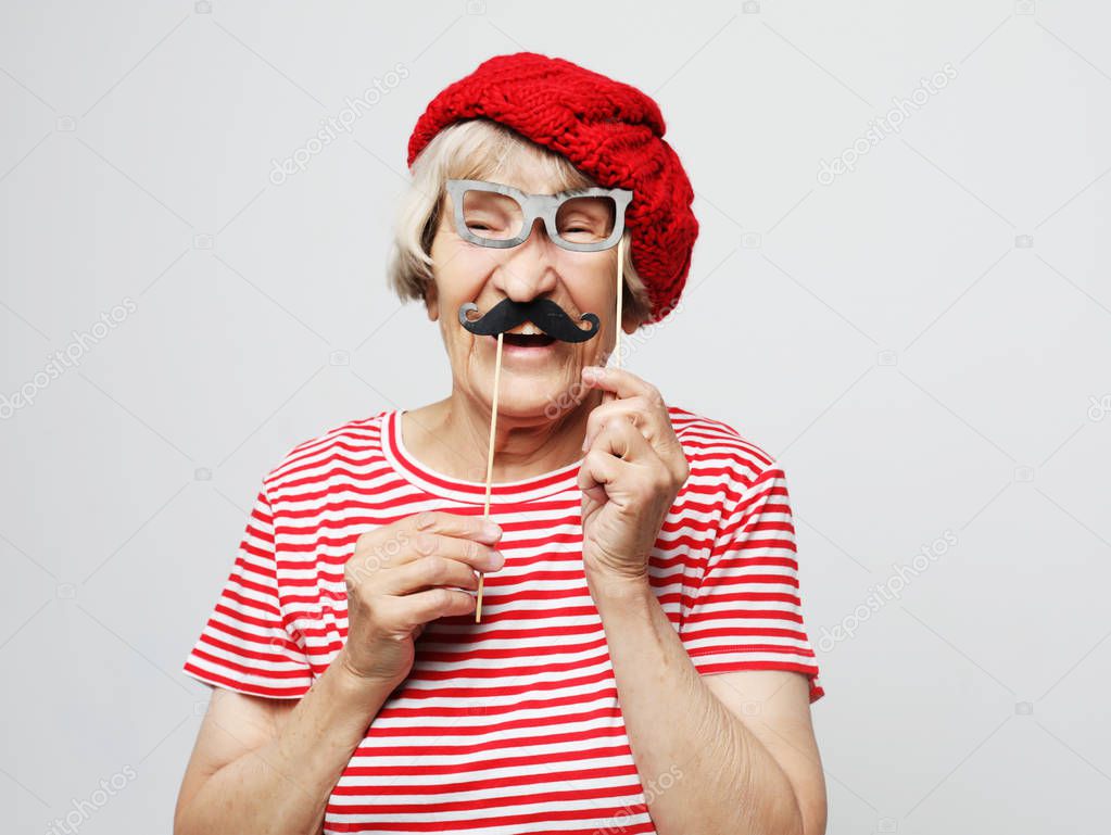 lifestyle and people concept: funny grandmother with fake mustache and glasses, laughs and prepares for party