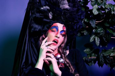 Moda, Güzellik, insanlar ve Cadılar Bayramı kavramı: parlak bir yaratıcı makyaj ve büyük bir siyah headdress olan kadın.