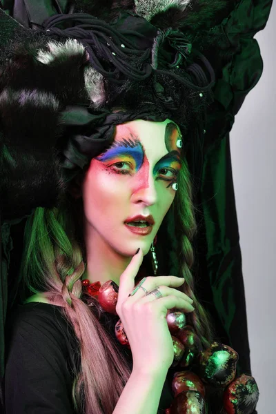 Moda, belleza, gente y concepto de Halloween: Mujer joven con un maquillaje creativo brillante y un gran tocado negro . — Foto de Stock