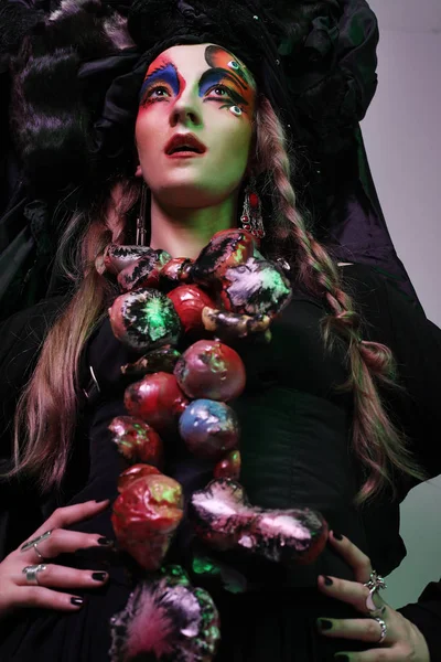 Mode, Schönheit, Menschen und Halloween-Konzept: junge Frau mit grellem, kreativem Make-up und großer schwarzer Kopfbedeckung. — Stockfoto